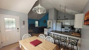 A modern kitchen with white cabinets, a wooden dining table with four chairs, and a hanging light fixture. - OBX~Beach~Sunsets~Bike Path~Mini Golf~Seafood~Shops~All within 1/2 mile away (Kill Devil Hills)