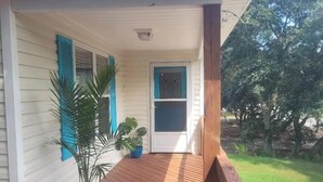 A covered porch with a wooden deck, a potted plant, and a door with blue shutters. - OBX~Beach~Sunsets~Bike Path~Mini Golf~Seafood~Shops~All within 1/2 mile away (Kill Devil Hills)