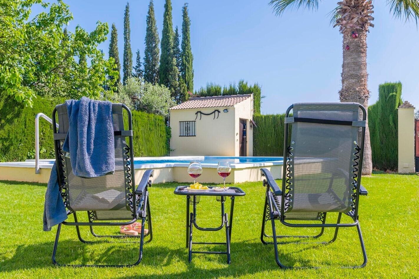 Zwei Gartenstühle mit Handtüchern, ein Schwimmbecken und ein kleines Gebäude mit einem Ziegeldach.
