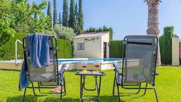 Zwei Gartenstühle mit Handtüchern, ein Schwimmbecken und ein kleines Gebäude mit einem Ziegeldach.