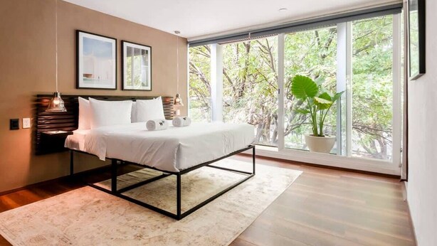 A modern bedroom with a bed, large windows, and a view of greenery. - w* | Enchanting 1BR w/ Terrace in Prime Polanco (Ciudad de México)