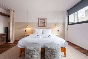 Quarto de hotel moderno com uma cama grande, duas mesas de cabeceira, um quadro na parede e uma janela com vista.