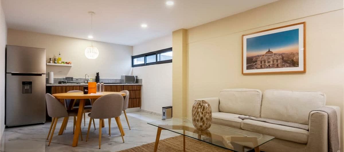 Una sala de estar moderna con una mesa de centro de vidrio, un sofá color beige y un comedor con una mesa y sillas de madera.