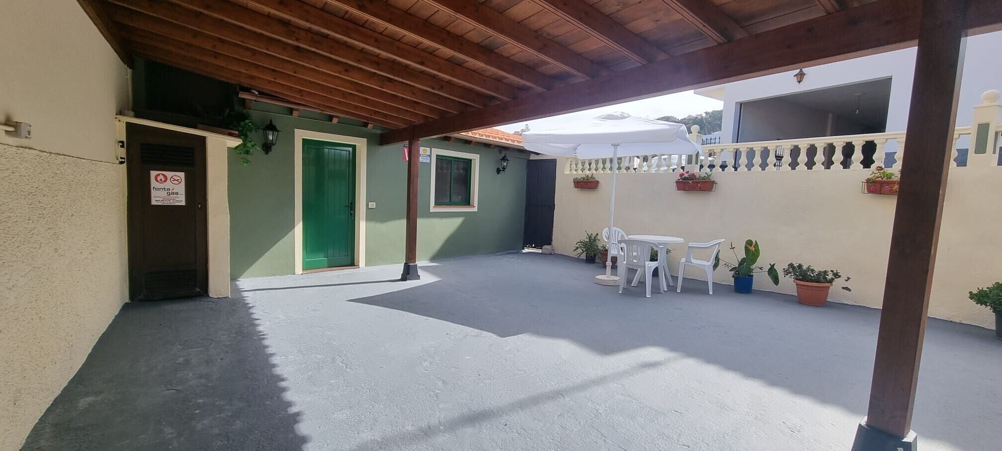 A covered outdoor area with a table and chairs, potted plants, and a green door.