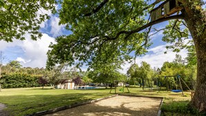 A park with a swing set, a sandbox, and a treehouse. - Vacation Home "Gite Senguinous 1" with Shared Pool, Private Terrace & Wi-Fi (Lesparre-Médoc)
