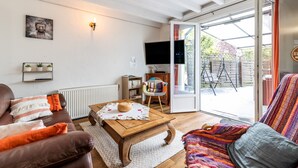 A living room with a sofa, a coffee table, a television, and a sliding glass door leading to an outdoor area. - Vacation Home "Gite Senguinous 1" with Shared Pool, Private Terrace & Wi-Fi (Lesparre-Médoc)