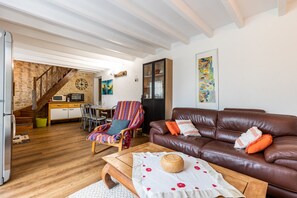 A cozy living room with a brown leather sofa, a wooden coffee table, a striped armchair, and a kitchen in the background. - Vacation Home "Gite Senguinous 1" with Shared Pool, Private Terrace & Wi-Fi (Lesparre-Médoc)
