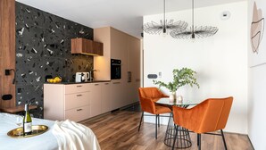 Una cuina moderna amb salabost a negre, armaris de fusta i zona de menjador amb cadires taronja i taula de vidre.
