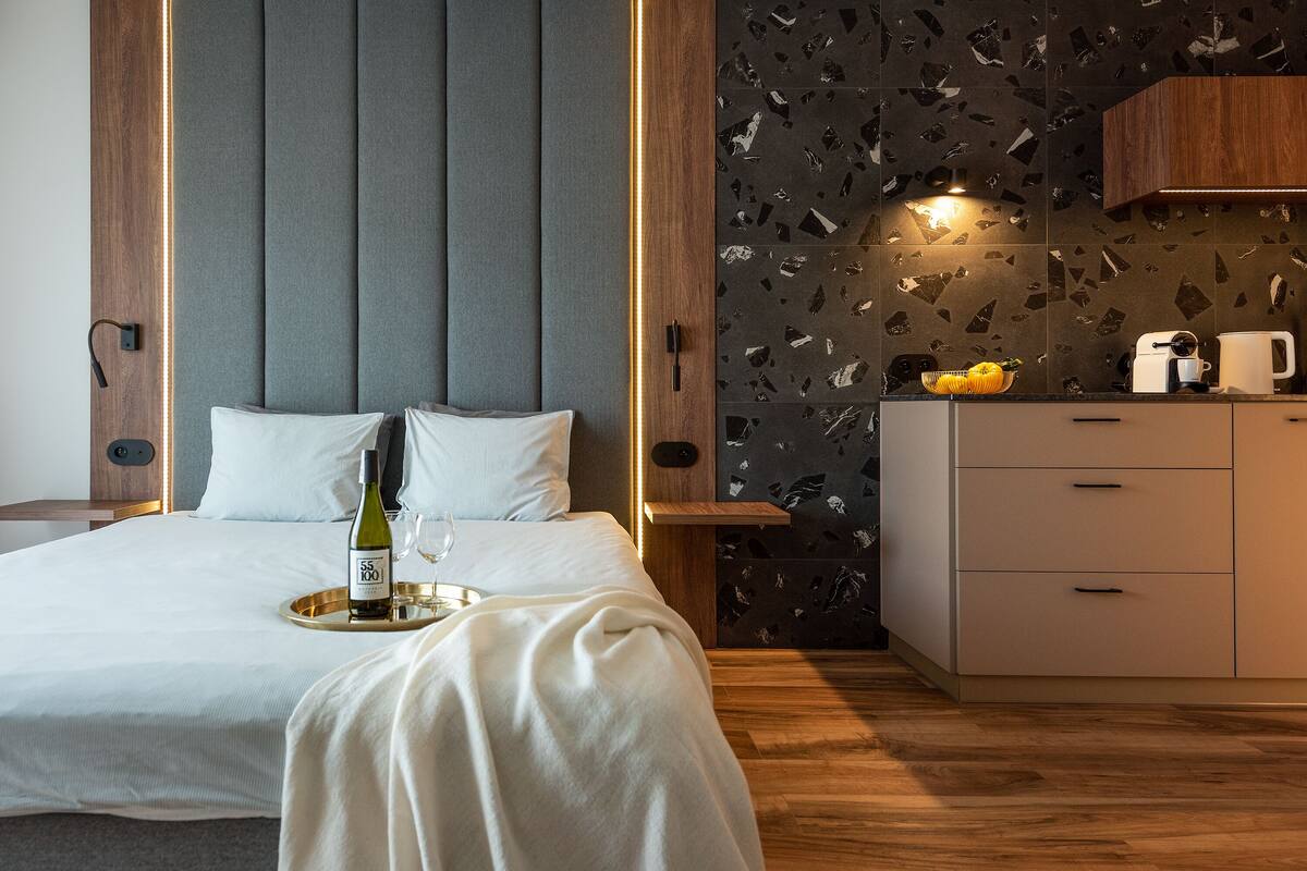 Een moderne hotelkamer met een bed, nachtkastje en een kleine kitchenette.