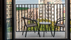 Un balcó amb dues cadires de vimetina i una taula rodona petita, amb vista a un paisatge urbà ple d'edificis d'altes plantes.