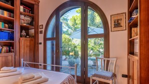 Un dormitorio con un amplio ventanal de arco, una cama con toallas, una silla y una estantería.