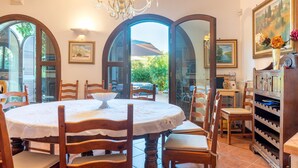 Un comedor con una mesa redonda, sillas de madera, un candelabro y vistas a través de puertas de cristal arqueadas.