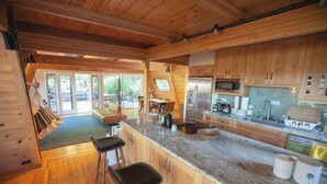 A modern kitchen with wooden cabinets, a marble countertop, and a dining area with a view. - Luxurious Bayview Treehouse: Hot Tub, 15 min to SF (Brisbane)