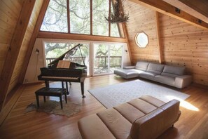 A loft-style room with a grand piano, a sofa, and a large window.