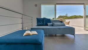 A modern bedroom with a large bed, a reading area, and a balcony with a view. - Villa Serena vista mare (Lacona)