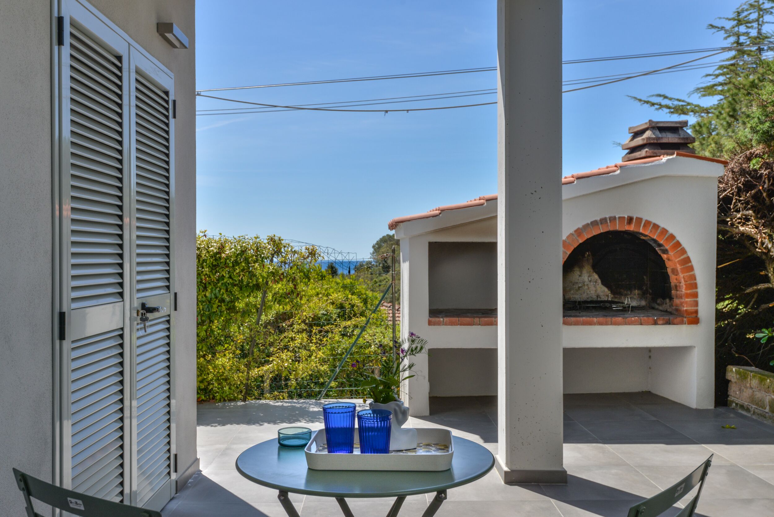 Eine Terrasse im Freien mit Tisch, blauen Gläsern und einem Backofen aus Ziegeln.