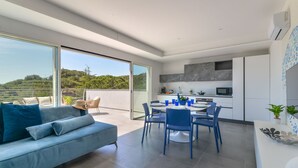 A modern kitchen with a dining area, large sliding glass doors, and a view of a green landscape. - Villa Serena vista mare (Lacona)