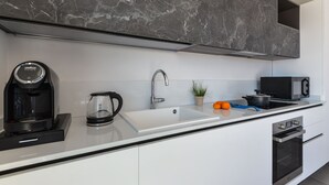 A modern kitchen with a white countertop, a coffee maker, a kettle, a sink, a microwave, and a stove. - Villa Serena vista mare (Lacona)