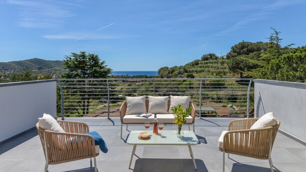 A rooftop terrace with a sofa, two wicker chairs, a table with a vase, and a view of the landscape. - Villa Serena vista mare (Lacona)