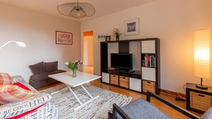 Una sala de estar con un sofá, una mesa de centro, un televisor, una estantería y una lámpara.