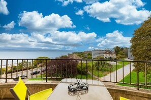 Ein Balkon mit Tisch, Stühlen und Blick auf das Meer und die Gebäude.