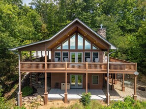 Une cabane en rondins dotée d’un balcon, de grandes fenêtres et d’une cheminée en pierre.
