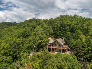 A two-story house with a porch, surrounded by dense forest. - Carie's Cabin-Mountain Views - Hot Tub - Gas Fireplace- 4WD/AWD (Bryson City)