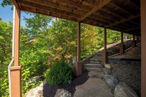 A covered wooden walkway with stone steps leading up a hill, surrounded by trees and shrubs.