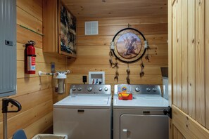 A laundry room with two Maytag washers and dryers, a fire extinguisher, a wall-mounted heater, and a dreamcatcher.