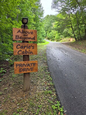 Un panneau indicateur en bois, doté de plusieurs flèches indiquant différentes directions, notamment « Above and Beyond », « Carie’s Cabin » et « CHEMIN PRIVÉ ».
