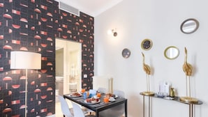 Ein moderner Essbereich mit einer Wand in Schwarz und Rot mit Muster, einem runden Spiegel und dekorativen, goldenen Vogel-Skulpturen auf einer Konsolentisch.