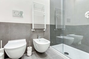 A modern bathroom with a toilet, bidet, and a glass-enclosed shower area.