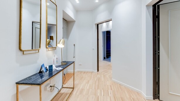 Un couloir moderne avec un comptoir en marbre noir, des miroirs encadrés d’or et un lampadaire.