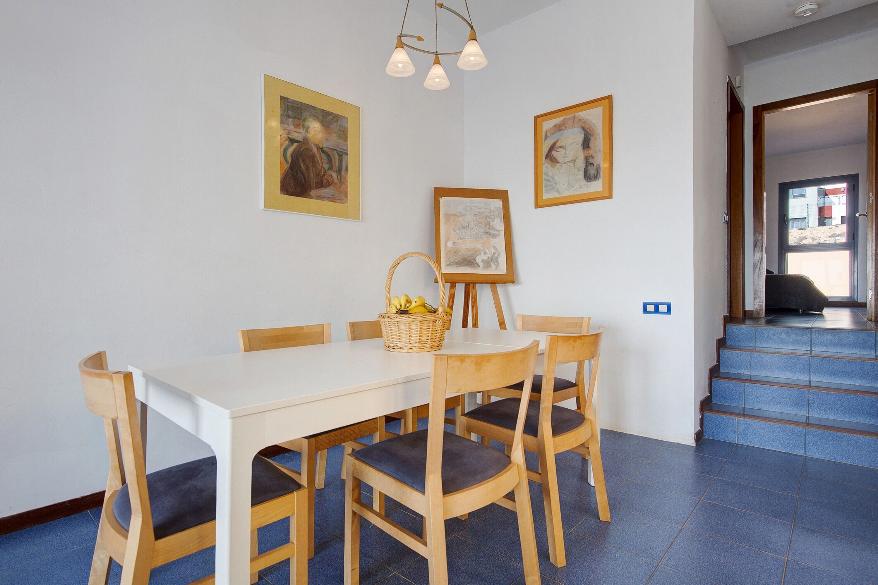 A dining area with a white table, wooden chairs, and framed artwork on the walls.