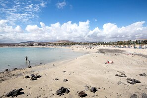 Una playa con agua cristalina, rocas y algunas personas.