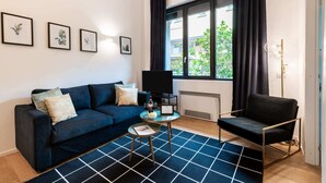 Ein modernes Wohnzimmer mit einem dunkelblauen Sofa, einem Couchtisch, einem schwarzen Sessel und einem großen Fenster mit Vorhängen.