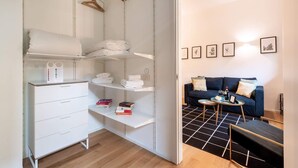 Ein Zimmer mit einem weißen Kleiderschrank, Regalen mit gefalteten Handtüchern, einem kleinen Tisch mit einer Schale und einem blauen Sofa mit Kissen.