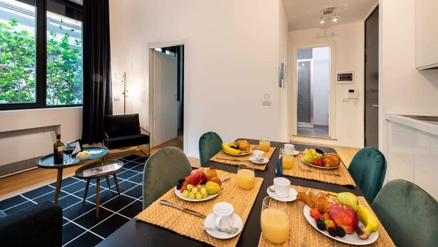 Ein modernes Hotelzimmer mit Essbereich und Frühstücksbuffet mit Früchten, Gebäck und Saft.