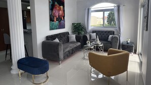 Una sala de estar moderna con un sofá gris, un reposapiés azul y un sillón marrón. Hay un ventanal con vistas a edificios.