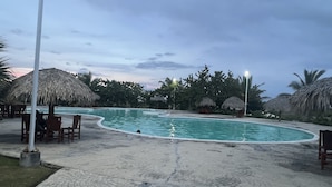 Una piscina con borde curvo, rodeada de sillas de descanso y sombrillas de paja.