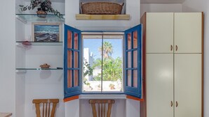 Ein Zimmer mit Fenster, zwei Stühlen, einem Kleiderschrank und Regalen mit verschiedenen Gegenständen.