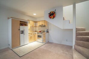 A compact kitchen with a refrigerator, stove, and cabinets, leading to a staircase.