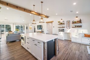 Uma cozinha moderna com uma ilha grande, vigas de madeira, iluminação pendente e uma área de refeições com sofá.