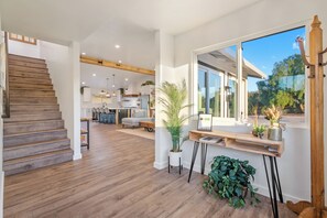 A modern interior with a wooden staircase, a kitchen area, and a large window with a view.