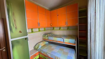 Une petite pièce comprenant deux lits superposés, un petit bureau et une armoire aux panneaux orange et verts.