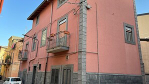 A multi-story building with balconies, a car parked in front, and a clear sky. - Apartment With Terrace Close to Catania, Sicily (Adrano)