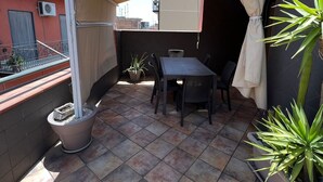 A covered patio area with a table and chairs, potted plants, and a view of the neighborhood. - Apartment With Terrace Close to Catania, Sicily (Adrano)