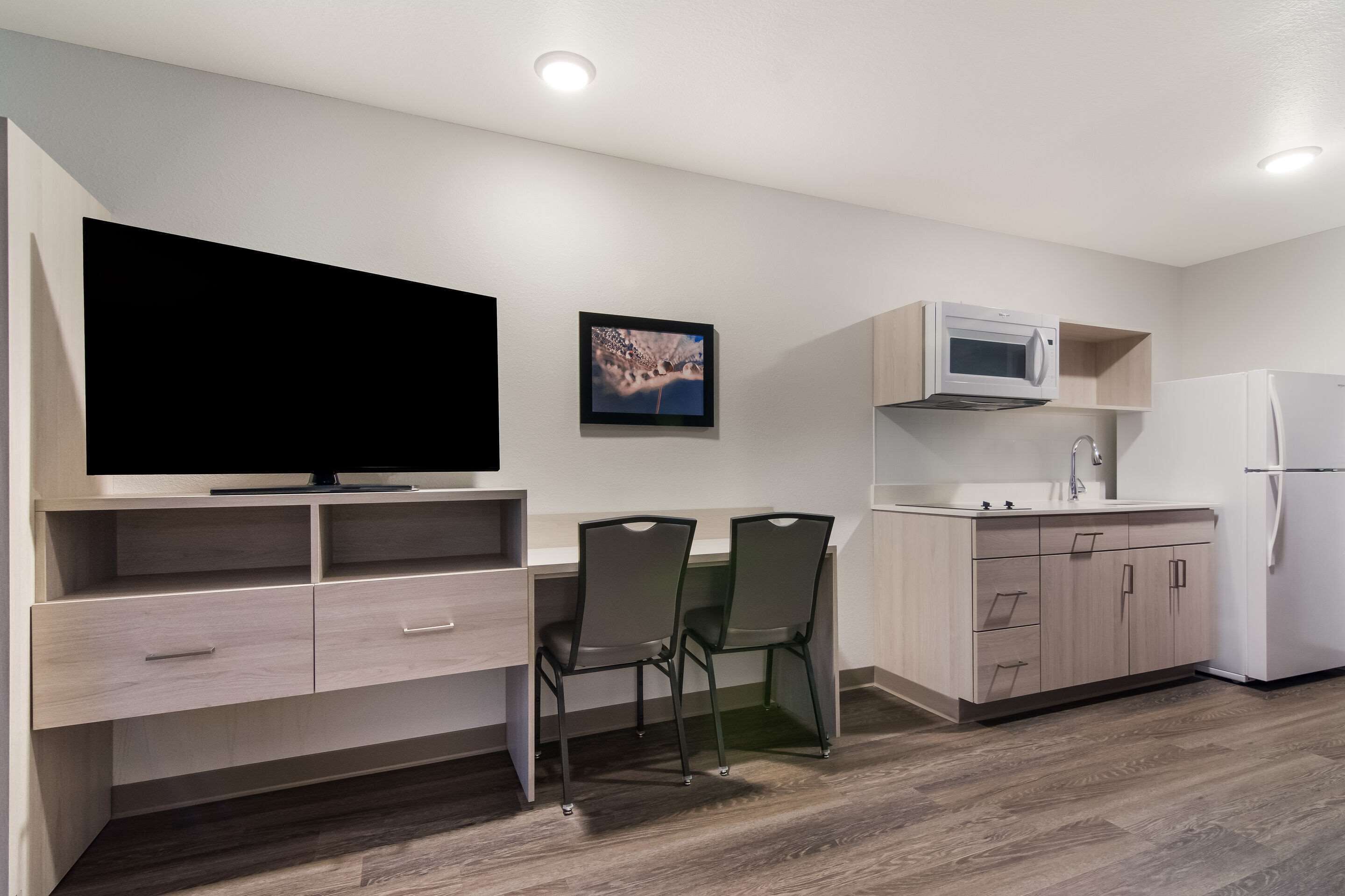 A modern kitchen with a flat-screen TV, two chairs, a microwave, and a refrigerator.
