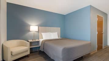 A hotel room with a bed, a nightstand, a lamp, a chair, and a wooden door.