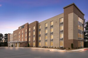 A hotel with a brick facade, multiple windows, and a parking lot. - WoodSpring Suites Morrisville Raleigh Durham Airport (Morrisville)